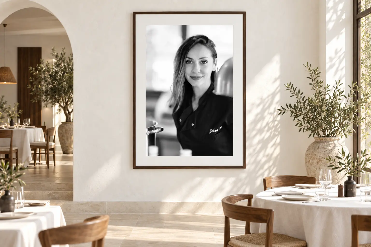 Ingelijst zwart-witportret van chef-kok Zohra aan een witte muur in een licht restaurantinterieur in Marbella-stijl