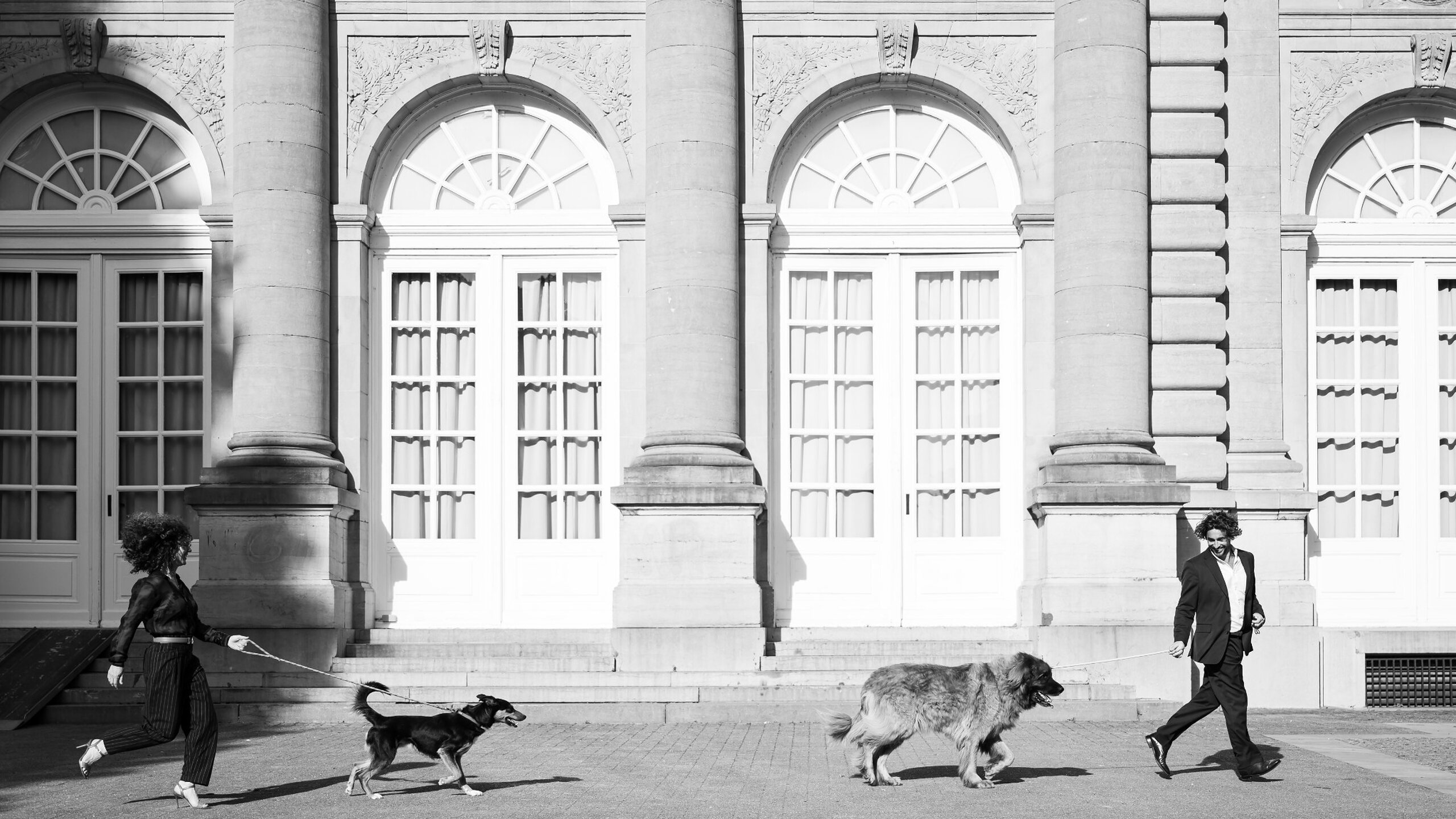 Architecturaal fine-artportret van klanten die met hun honden voor een klassieke gevel wandelen, door Bart Coenaers